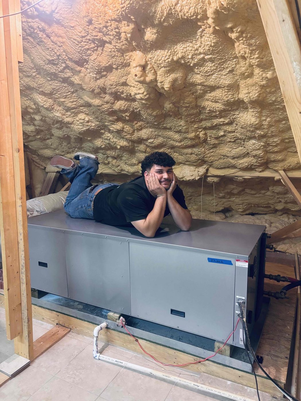 A technician resting on a new air handler in a spray-foam insulated attic