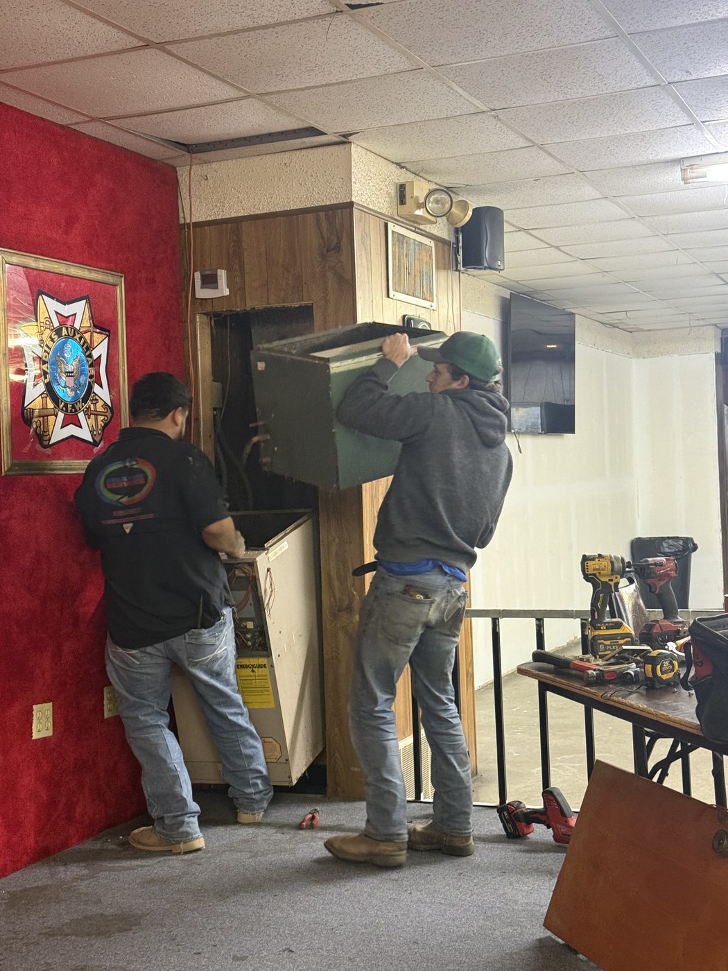 Two technicians lifting an old furnace out of a wall closet at a veterans' hall