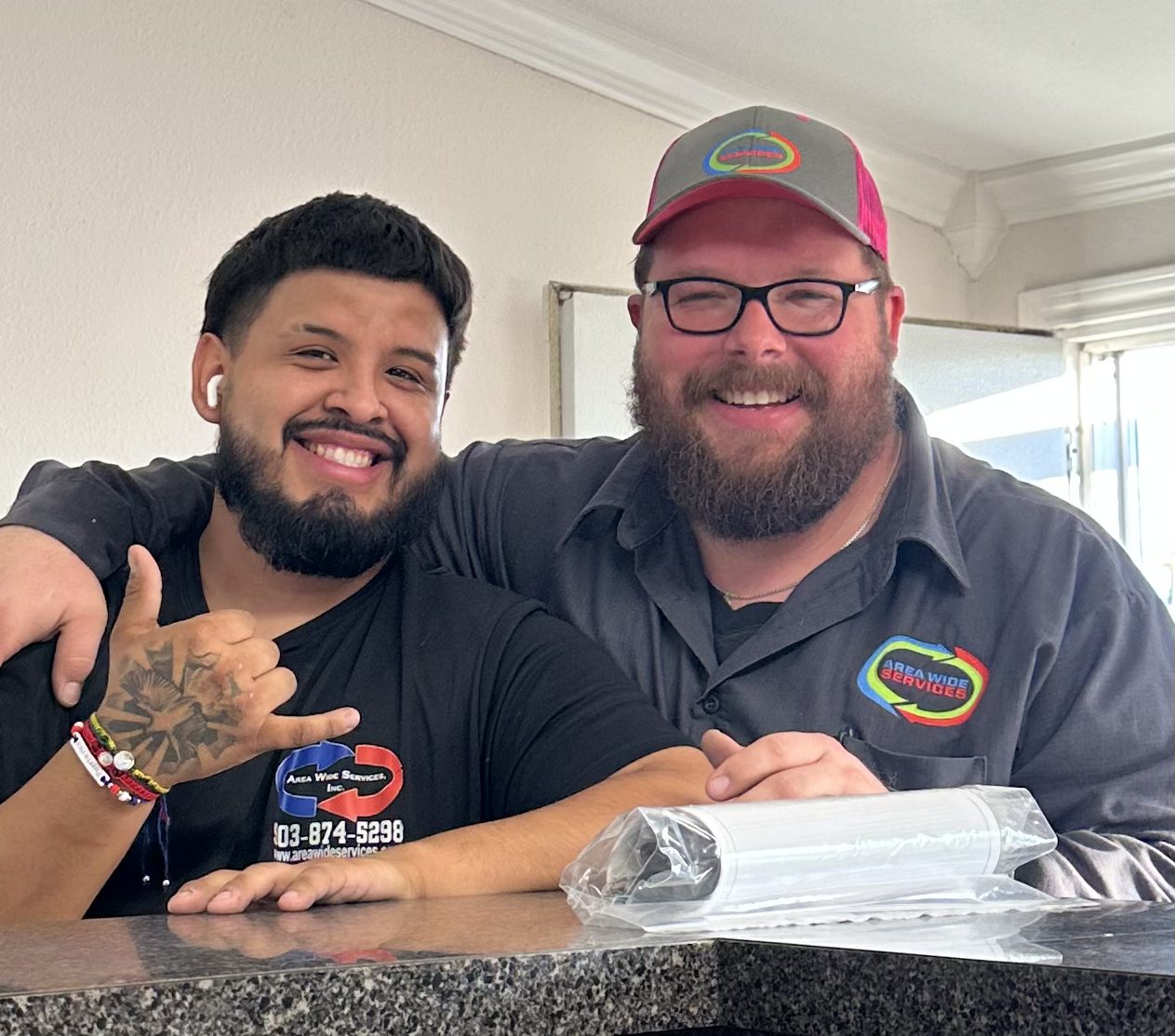 Two smiling Area Wide Services technicians in branded shirts
