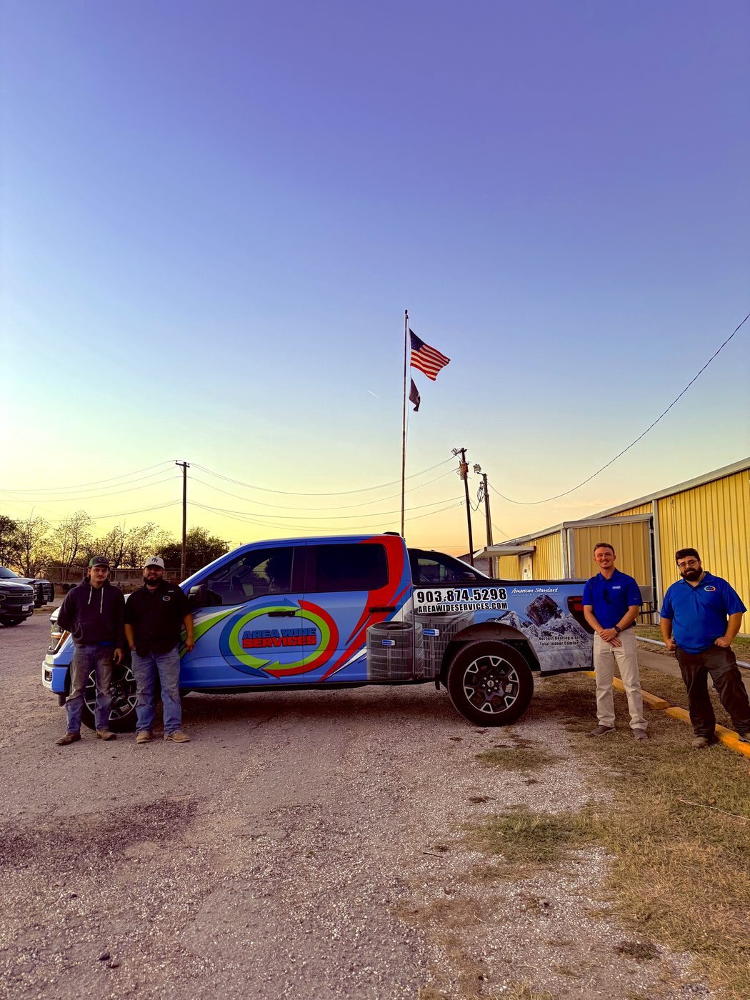 Four Area Wide Services crew members standing with a company truck wrapped in the Area Wide Services logo at sunset