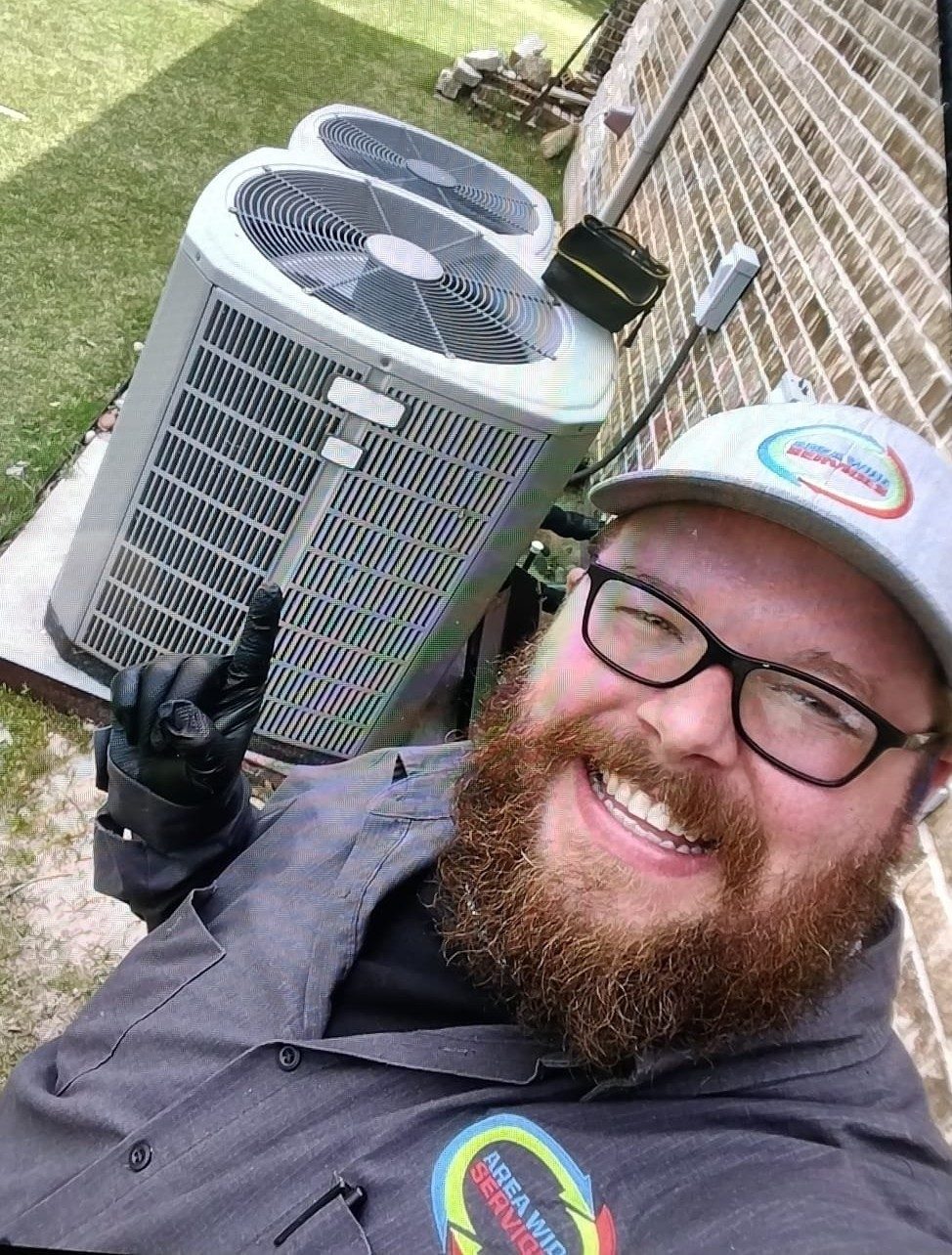 A smiling technician in a company cap giving a thumbs-up beside two air conditioning units